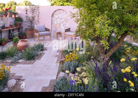 Un mur de calcaire derrière une terrasse pavée et un chemin entouré de plantes tolérantes à la sécheresse dans le jardin Meditrraneo. Designer : Katerina Kanatal Banque D'Images