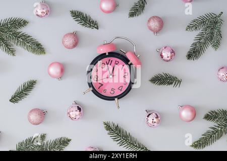 Motif de Noël tendance créatif fait avec des boules de Noël roses, des branches d'arbre de Noël enneigées vertes et un réveil rose sur fond gris. Banque D'Images