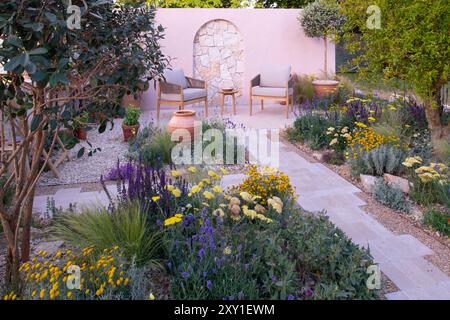 Un mur de calcaire derrière une terrasse pavée et un chemin entouré de plantes tolérantes à la sécheresse, y compris Achillea 'Moonshine', Salvia nemerosa 'Carado Banque D'Images