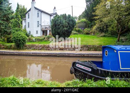 Homme pilotant un bateau étroit de canal passant devant un chalet au bord du canal sur le canal Shropshire Union canal à Tiverton près de Bunbury Cheshire Banque D'Images