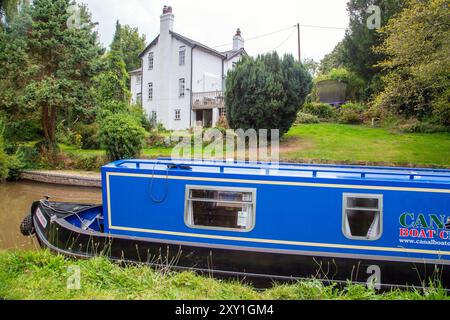 Homme pilotant un bateau étroit de canal passant devant un chalet au bord du canal sur le canal Shropshire Union canal à Tiverton près de Bunbury Cheshire Banque D'Images