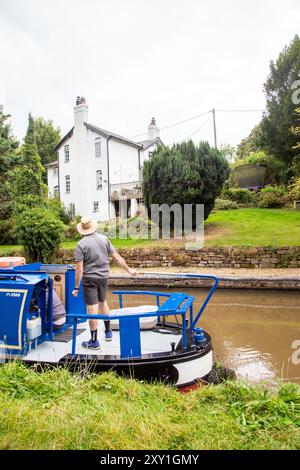 Homme pilotant un bateau étroit de canal passant devant un chalet au bord du canal sur le canal Shropshire Union canal à Tiverton près de Bunbury Cheshire Banque D'Images