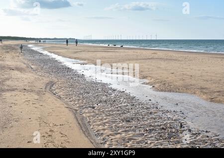 Sable, pierres et motifs de galets, et piscines d'eau laissées par la marée qui recule sur la plage de Marske by the Sea, avec Redcar Wind Farm visible à l'horizon. Banque D'Images