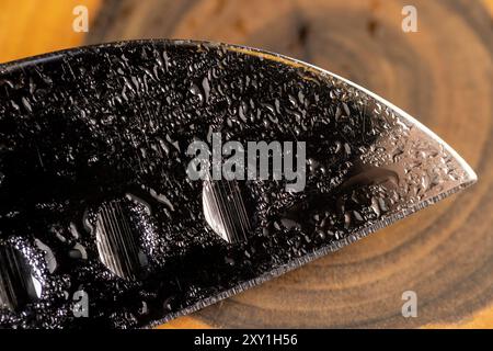 couteau recouvert de gouttelettes d'eau sur un fond de tableau noir, une lame humide d'un couteau tranchant avec une lame large Banque D'Images