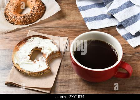 Une tasse de café fraîche et un bagel avec du fromage à la crème sur une table en bois. Banque D'Images