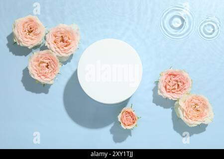 Belles fleurs de rose et podium de forme ronde dans l'eau sur fond bleu clair, pose plate Banque D'Images