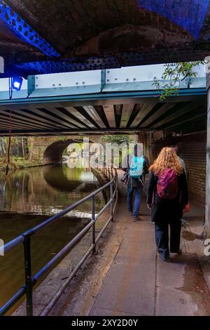 Amis marchant à visiter avec une caméra se promenant dans un tunnel de pont sur la promenade du canal Regent dans le quartier résidentiel de Maida Vale, Banque D'Images