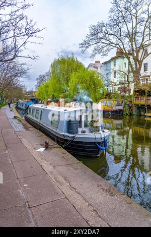 Femme courant le long de la promenade du Regent's canal dans la petite Venise de Londres avec des péniches étroites colorées amarrées et amarrées sur la rivière dans le reste Banque D'Images