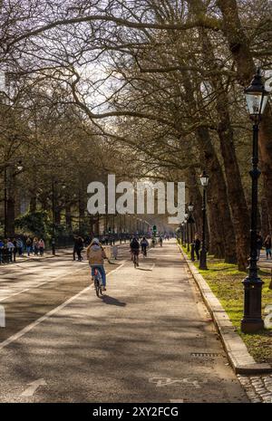 Les gens marchent et font du vélo sur la piste cyclable de Constitution Street Hill dans Buckingham Palace Garden magnifiquement illuminé par la lumière du soir. Banque D'Images