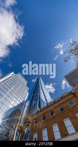 Vue en angle bas du gratte-ciel en verre en forme de pyramide moderne The Shard avec le ciel bleu et quelques nuages reflétés dans les fenêtres des bâtiments avec le soleil réfléchi Banque D'Images