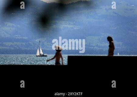 Nonnenhorn, Allemagne. 27 août 2024. Un voilier vogue derrière les baigneurs à travers le lac de Constance, scintillant au soleil. Crédit : Karl-Josef Hildenbrand/dpa/Alamy Live News Banque D'Images