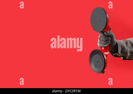 Main femelle dans un gant tenant deux ventouses à vide sur fond rouge Banque D'Images
