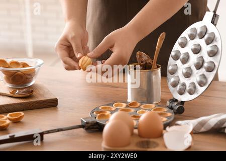 Femme cuisinant de savoureux biscuits en forme de noix avec du lait condensé bouilli à la table en bois dans la cuisine Banque D'Images