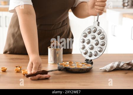 Femme cuisinant de savoureux biscuits en forme de noix avec du lait condensé bouilli à la table en bois dans la cuisine Banque D'Images