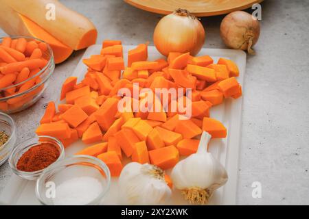 Gros plan de courge musquée pelée et hachée, carotte, ail et oignon. Recette de soupe de courge musquée, ingrédients sur une table de cuisine Banque D'Images