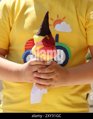 Un enfant tenant un cornet de crème glacée coloré trempé dans du chocolat. Banque D'Images