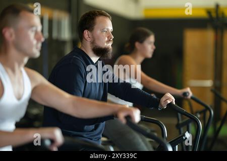 Un gars barbu qui fait de l'entraînement cardio sur vélo pneumatique dans la salle de gym Banque D'Images