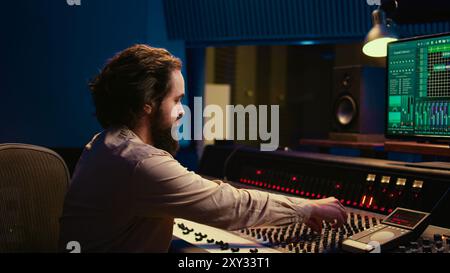 Portrait de producteur de musique travaillant dans un studio professionnel de salle de contrôle et d'édition d'enregistrements audio, console de mixage et logiciel daw dans un espace insonorisé. Ingénieur du son en post-production. Caméra B. Banque D'Images