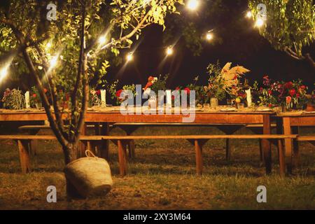 Table préparée pour un dîner en plein air rustique de nuit avec des fleurs, et des lampes wineglasses dans le jardin Banque D'Images