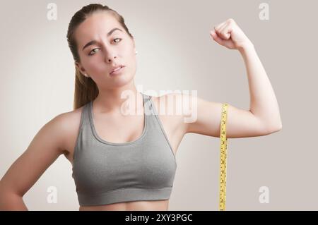 Femme puissante mesurant ses biceps avec un ruban jaune Banque D'Images