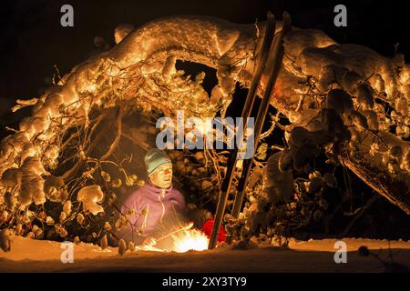 Homme griller des saucisses sur un feu de camp sous un pin enneigé, Gaellivare, Norrbotten, Laponie, Suède, novembre 2012, Europe Banque D'Images