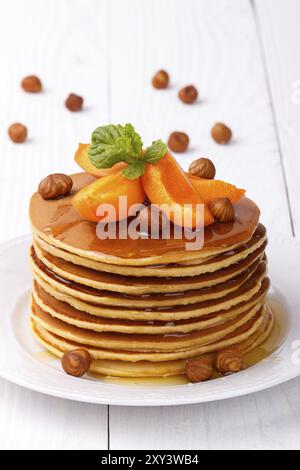 Pile de crêpes américaines maison servies avec miel, noisettes et abricots sur assiette blanche Banque D'Images