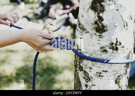 Les mains des femmes tirent une corde bleue forte attachée à un arbre de bouleau. Installation professionnelle de tyrolienne ou de téléphérique. Il est temps de s'amuser et de se détendre. Week-end en famille Banque D'Images