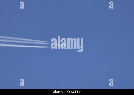 Avion géant Boeing 747 survolant un ciel bleu avec une traînée de vapeur ou une traînée derrière, Angleterre, Royaume-Uni, Europe Banque D'Images