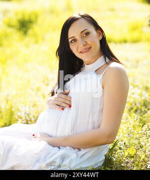 Magnifique Portrait de femme enceinte en robe blanche dans le parc printemps floraison Banque D'Images