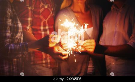 Groupe de personnes anonymes dans des vêtements décontractés brûlant des étincelles lumineuses pendant la fête la nuit Banque D'Images