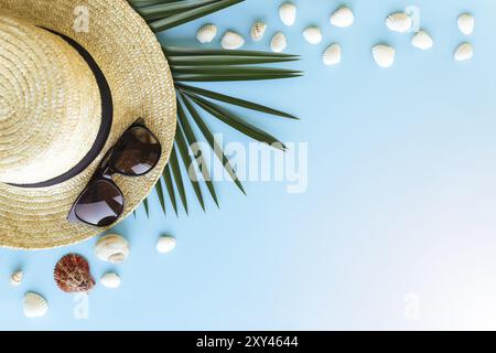 Voyage, concept de vacances. Chapeau avec coquillages, feuille de palmier et lunettes sur fond bleu. Banque D'Images