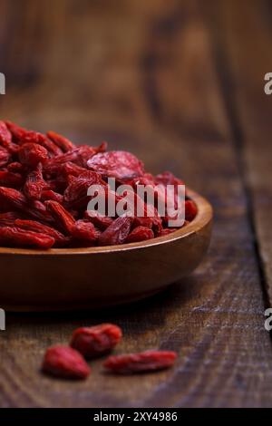 Baies de Goji dans un bol en bois sur une vieille planche rustique, mise au point sélective, macro Banque D'Images