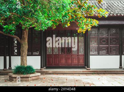 Architecture chinoise traditionnelle avec un grand arbre et des portes ornées à Suzhou, Chine. Banque D'Images