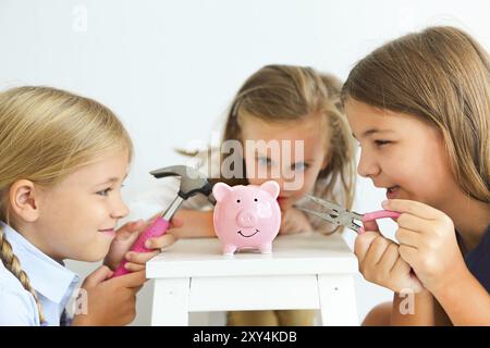 Les enfants à l'aide d'un tournevis, une pince et un marteau par la tirelire cochon rose sur fond blanc Banque D'Images