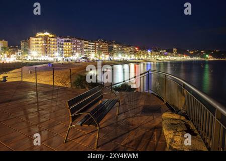 Lloret de Mar la nuit sur la Costa Brava en Catalogne, Espagne. Promenade avec banc et toits de la ville avec la réflexion en mer Méditerranée Banque D'Images