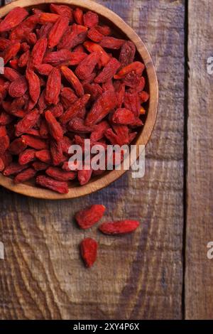 Baies de Goji dans un bol en bois sur une vieille planche rustique, mise au point sélective, macro Banque D'Images