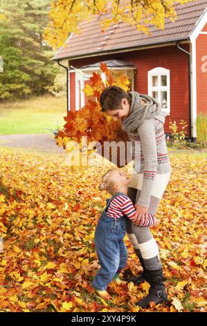 Jeune mère et sa petite fille ramassant les feuilles d'automne dans un panier devant une maison en bois peint en rouge typique en Suède et évidemment Havin Banque D'Images