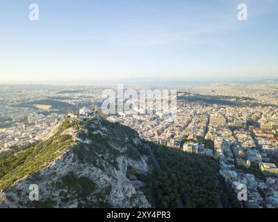 Vue aérienne par drone du mont Lycabette surplombant le paysage urbain jusqu'à la mer Méditerranée à Athènes, Grèce, Europe Banque D'Images