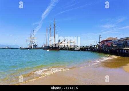 Plage au premier plan à côté de l'attraction touristique Hyde Street Pier avec des navires de style ancien amarrés à Fisherman's Wharf lors d'une journée d'été ensoleillée à San Francis Banque D'Images