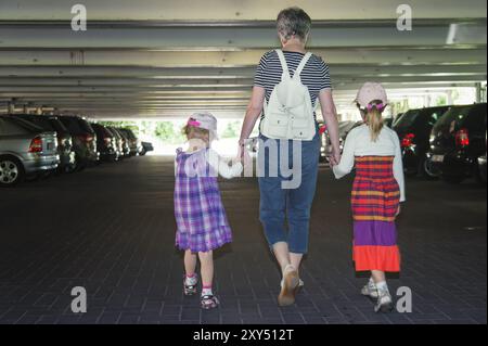 Une grand-mère marche main dans la main avec ses petites-filles dans un parking à plusieurs étages Banque D'Images