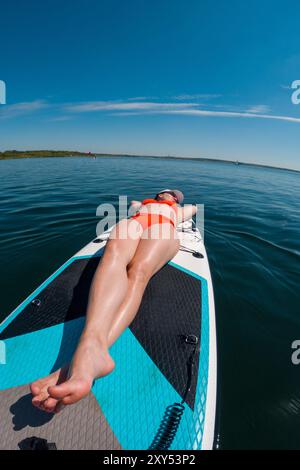 Femme se relaxant sur Paddleboard dans les eaux claires chaude journée d'été ensoleillée Banque D'Images