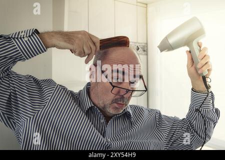 L'homme chauve se coiffe avec un peigne et un sèche-cheveux Banque D'Images