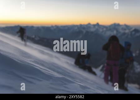 L'alpiniste floue équipé professionnellement à l'aube du soleil marche sur la pente tôt le matin et la neige dérive sur la neige au-dessus de la Banque D'Images