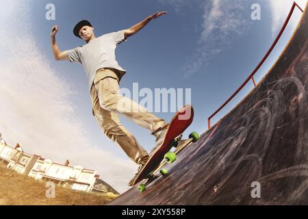 Adolescent patineur raccroché au-dessus d'une rampe sur une planche à roulettes dans un skate Park. Grand angle Banque D'Images