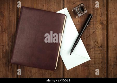 Une photo prise à la verticale d'un journal relié en cuir, une enveloppe bleue, une encre, stylo et bien tourné d'en haut sur un fond rustique foncé avec une place pour le texte Banque D'Images