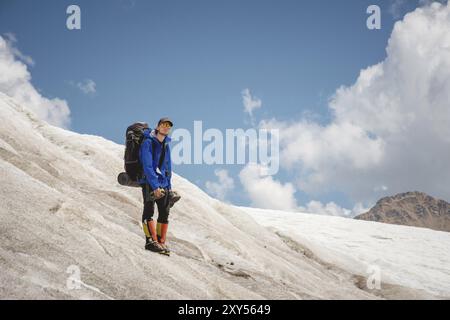 Un alpiniste avec un sac à dos marche en fauteuil roulant, se tient sur un glacier poussiéreux avec des baskets dans les mains entre les fissures dans les montagnes Banque D'Images