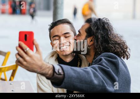 Deux hommes s'embrassant dans la rue, l'un d'eux tenant un téléphone rouge Banque D'Images