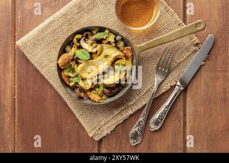 Une photo d'un champignons rustique et olives saute dans une poêle en fonte, avec un verre de vin blanc, tourné par le haut sur un fond rustique foncé avec l'exemplaire Banque D'Images