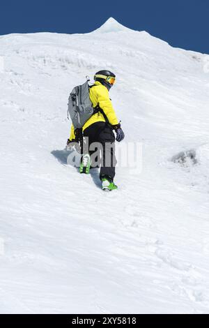 Un skieur dans un casque et un masque avec un sac à dos s'élève sur une pente contre le fond de neige et un glacier. Freeride de l'arrière-pays Banque D'Images