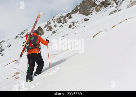 Le ski freerider grimpe la pente en poudreuse profonde avec l'équipement à l'arrière fixé sur le sac à dos. Le concept de sports extrêmes d'hiver Banque D'Images